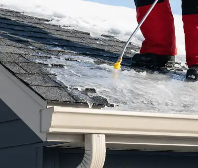 Ice dam removal technician using a steam wand to melt thick ice buildup on a residential roof in Denver, CO