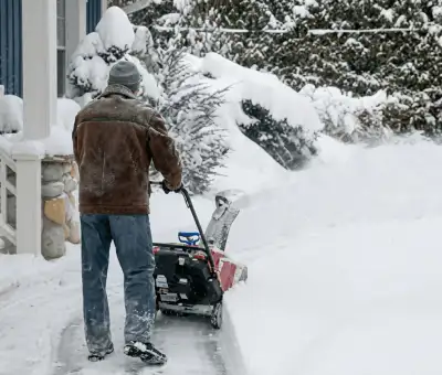 Residential snow removal technician using a snow blower to clear a home driveway and walkway in Denver, CO