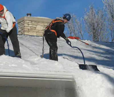 Professional technicians performing roof snow removal with safety harnesses and shovels in Denver, CO